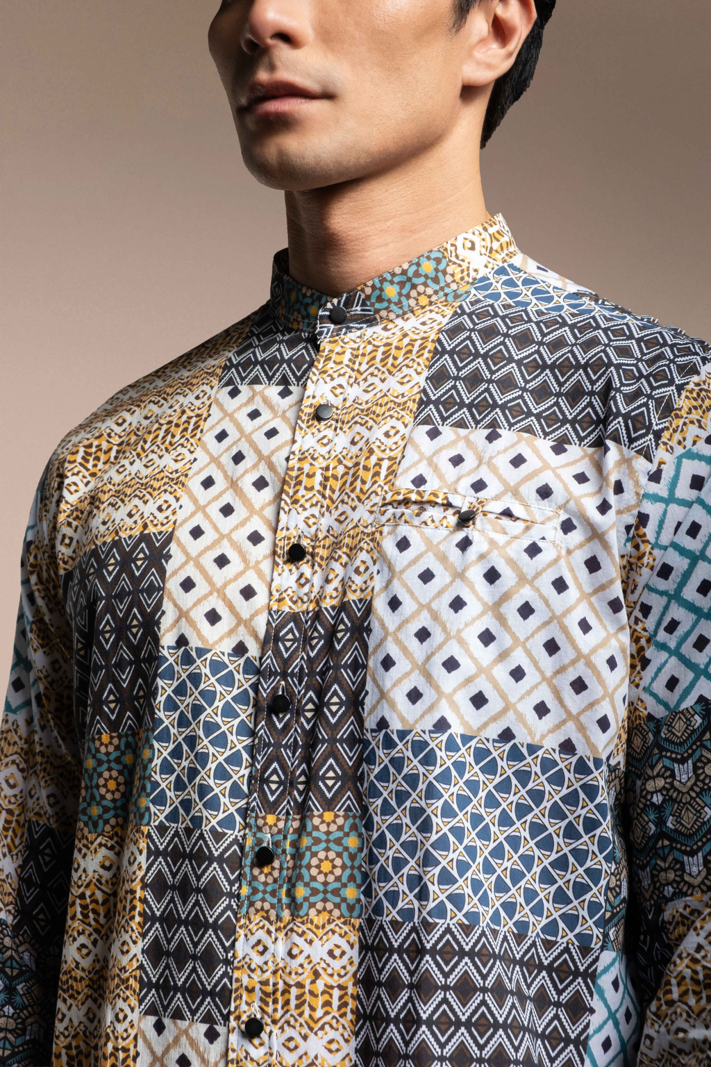 A close-up of a man wearing Onésimus Men's Casual Shirts: Geometric Prints shirt with a multicolor geometric patchwork print in blue, beige, white, and black.