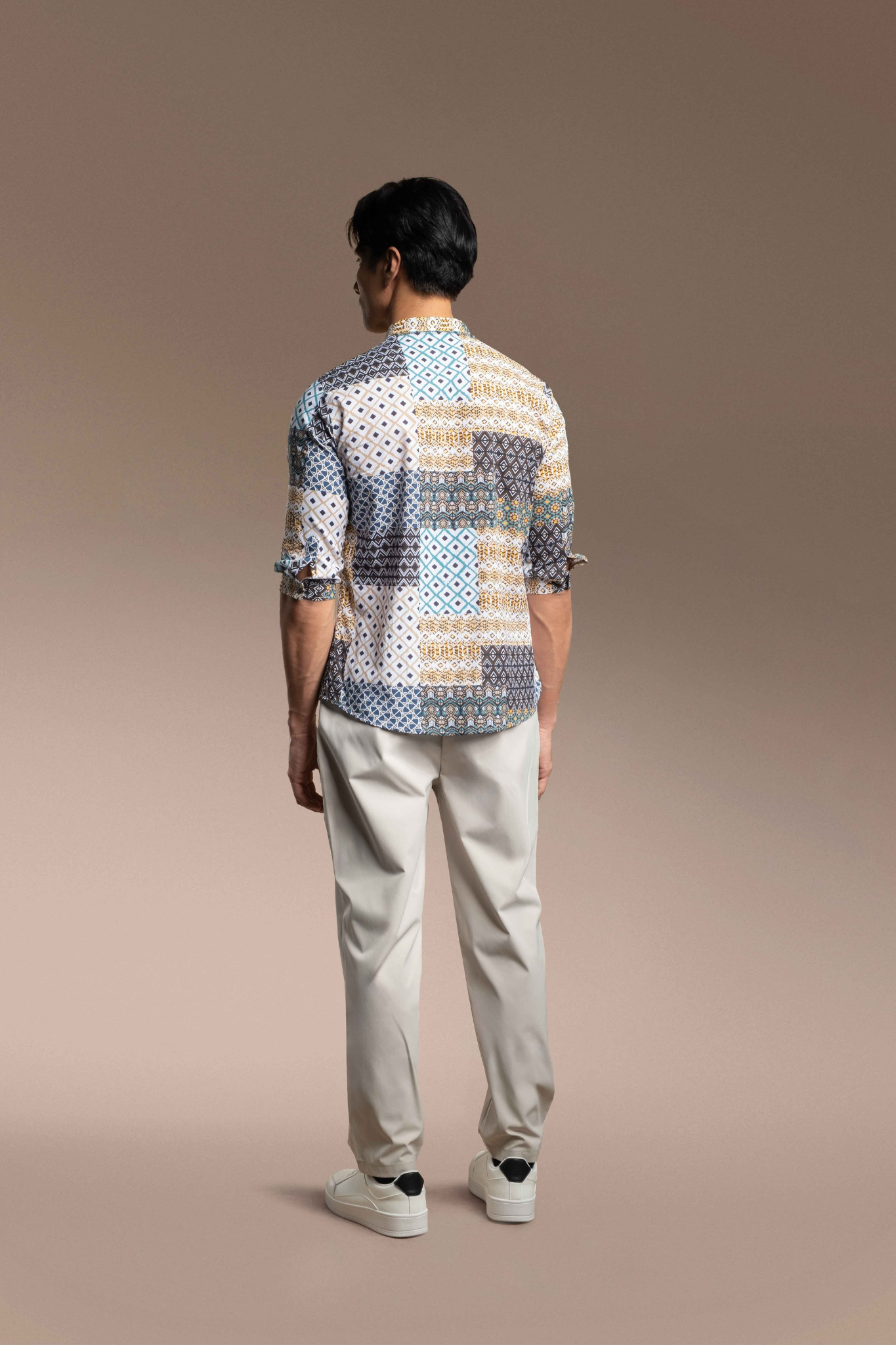 A man viewed from behind wearing Onésimus Men's Casual Shirts Geometric Prints, set against a solid warm brown studio background.